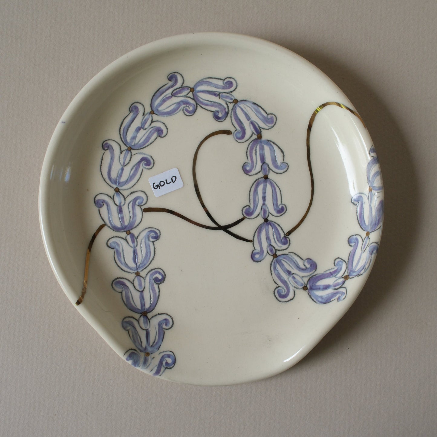Ceramic plate with purple crown flowers and gold detailing on a white stoneware spoon rest.