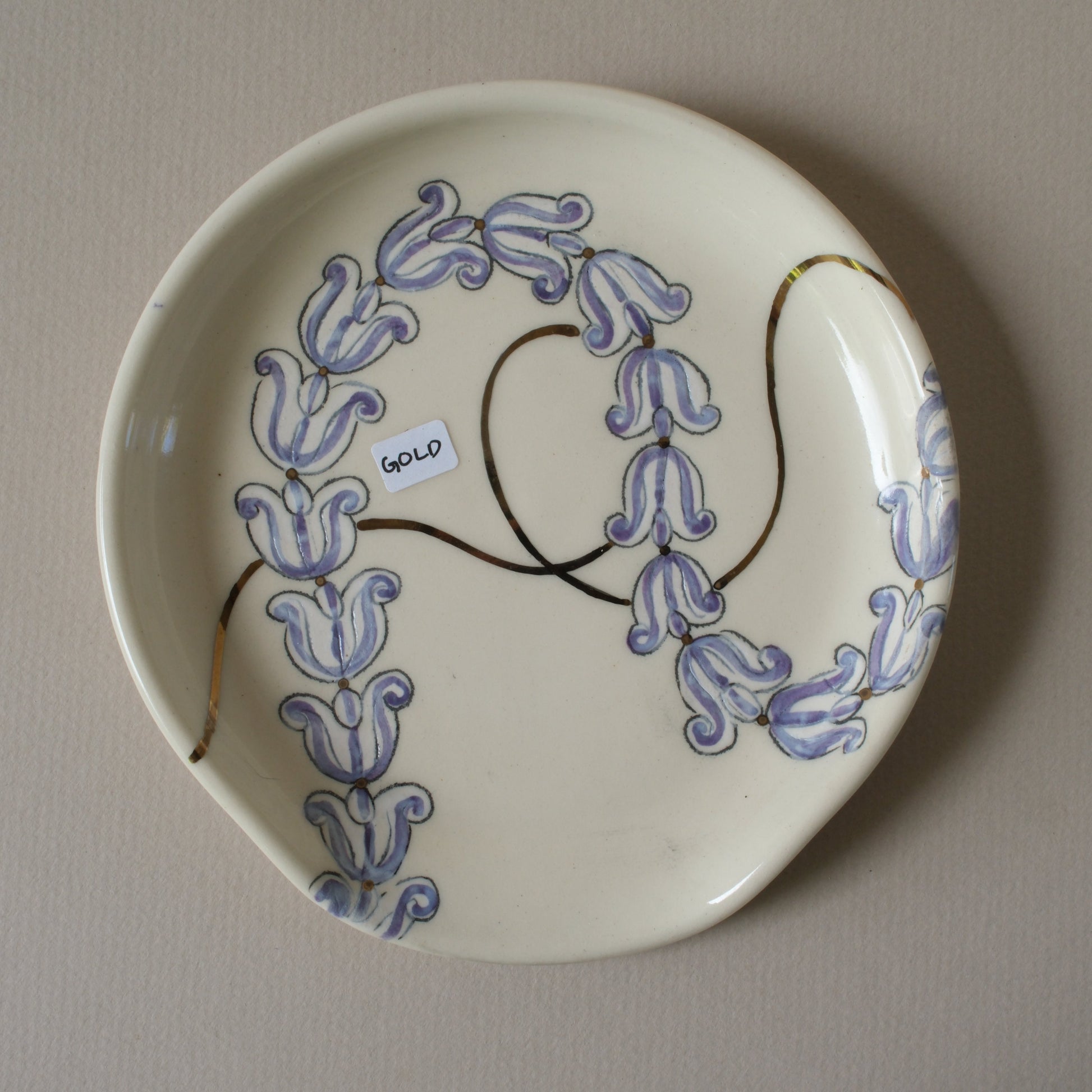 Ceramic plate with purple crown flowers and gold detailing on a white stoneware spoon rest.